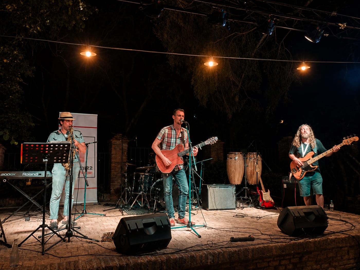 Banda tocando en directo sobre un escenario al aire libre, con monitores y microfonía