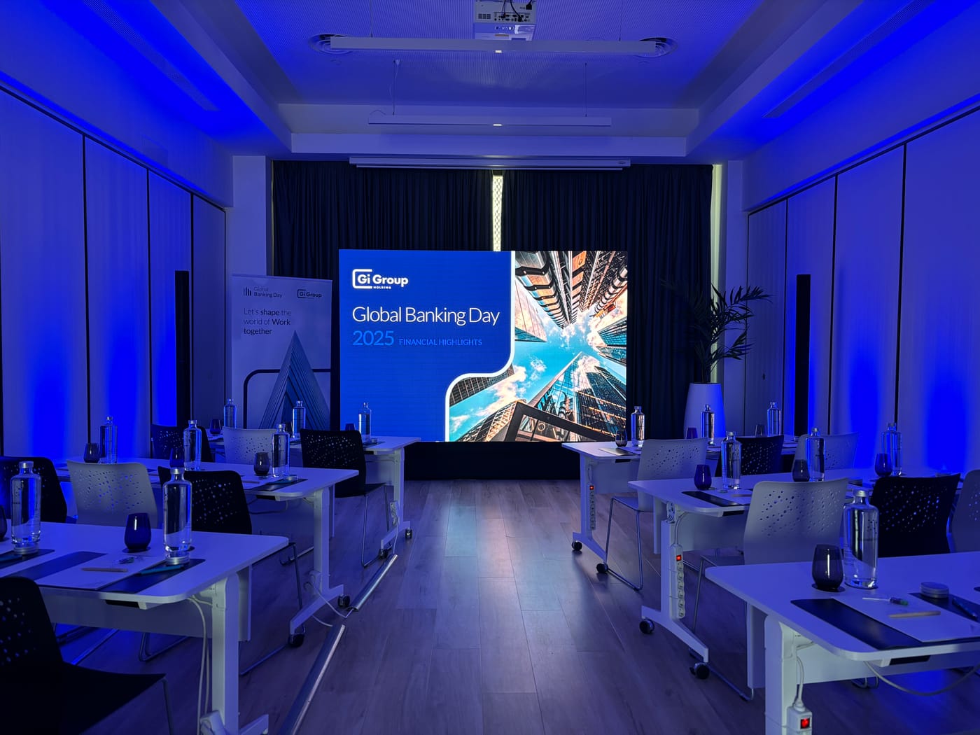 Pantalla LED montada al fondo de una sala de evento corporativo, con las mesas preparadas y luz azul de ambiente