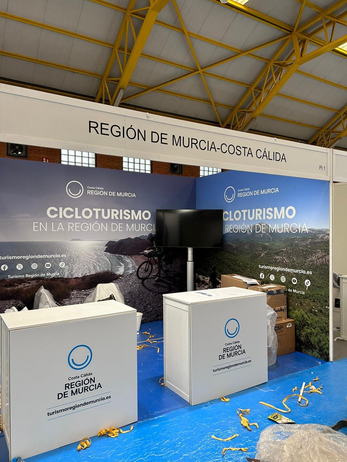 Televisor sobre soporte de suelo dentro de un stand de feria, junto a los paneles gráficos del expositor